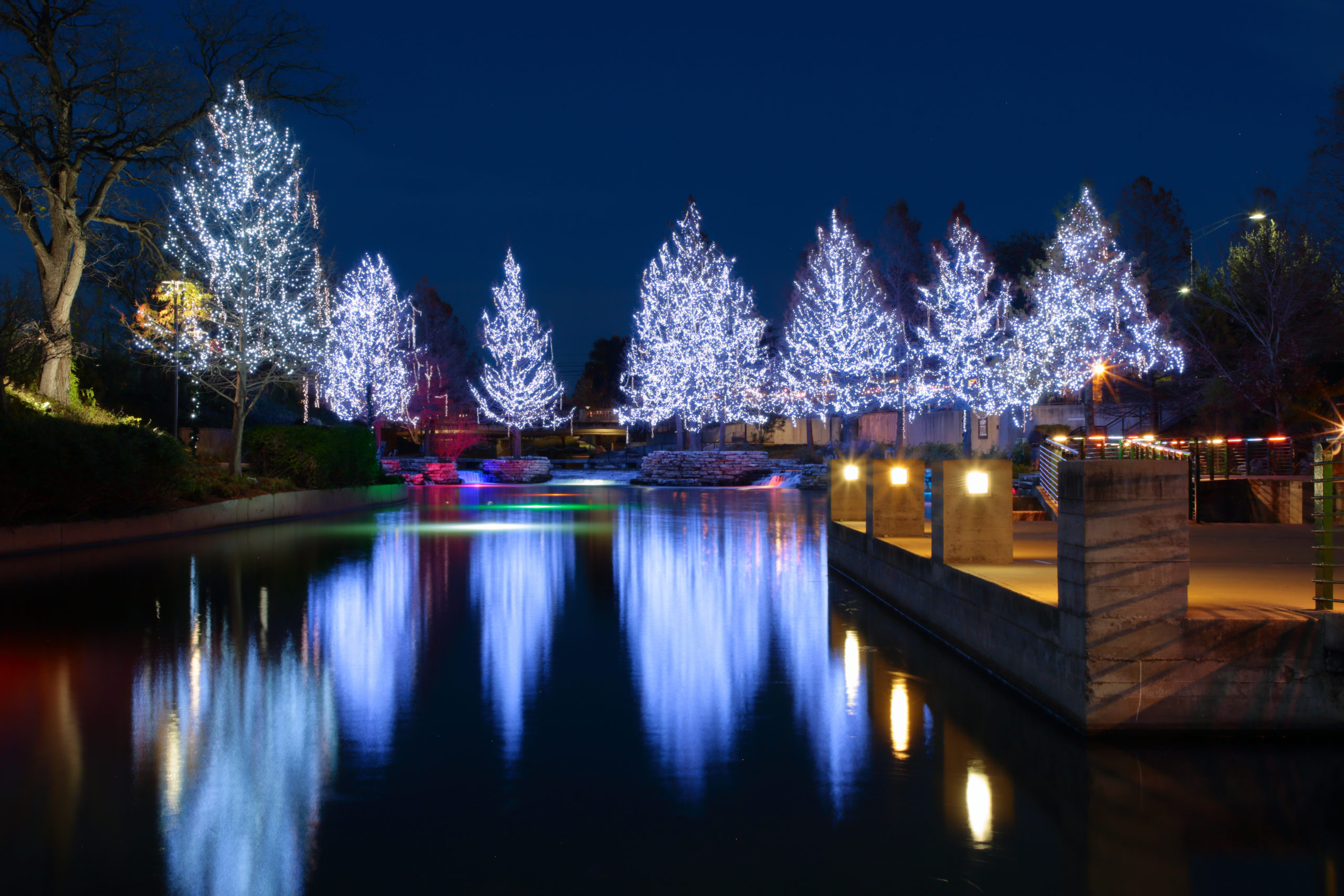 white christmas lights on trees reflected on water at san antonio riverwalk