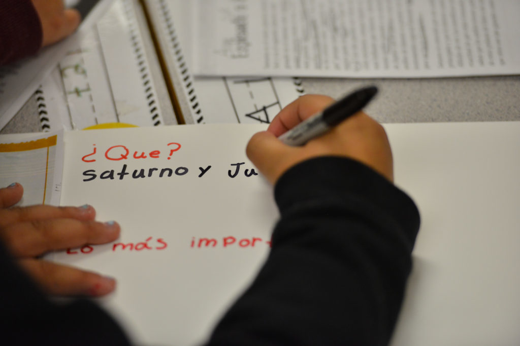 child's hand holding a marker and writing in Spanish