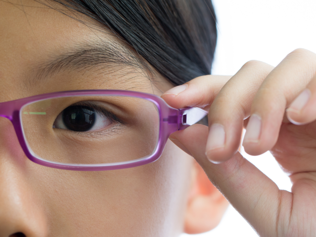 close up of child's eye and their hand holding purple glasses up to their face