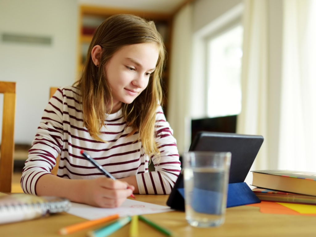 girl holding sitting at home desk holding pencil and looking at tablet