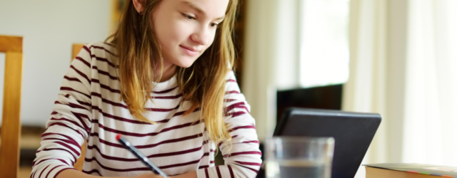 girl holding sitting at home desk holding pencil and looking at tablet for distance learning