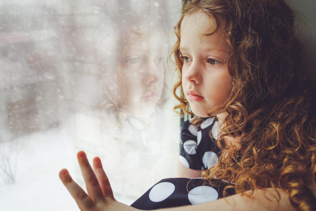 young girl looking sadly out window at snow