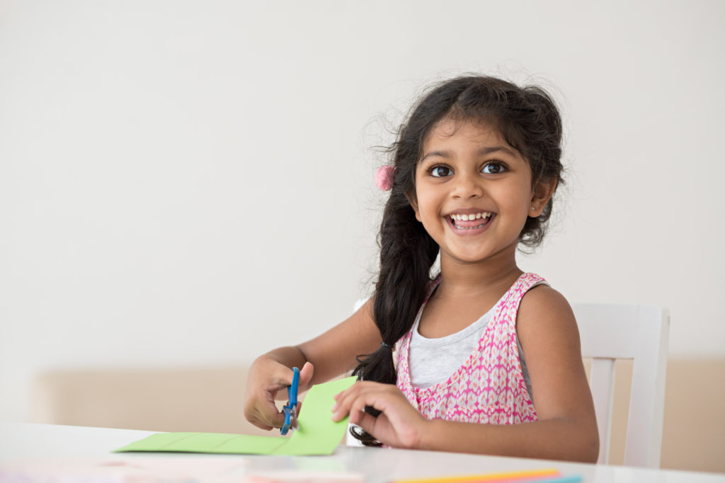 preschool girl smiling and cutting paper for preschool math activity
