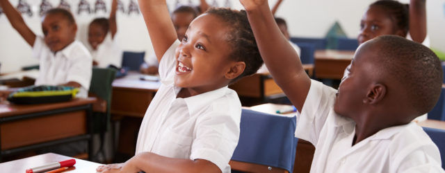 young students raising their hands in classroom