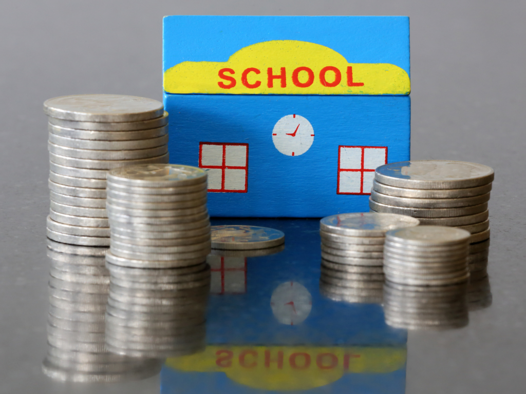 stacks of coins in front of blue toy school house