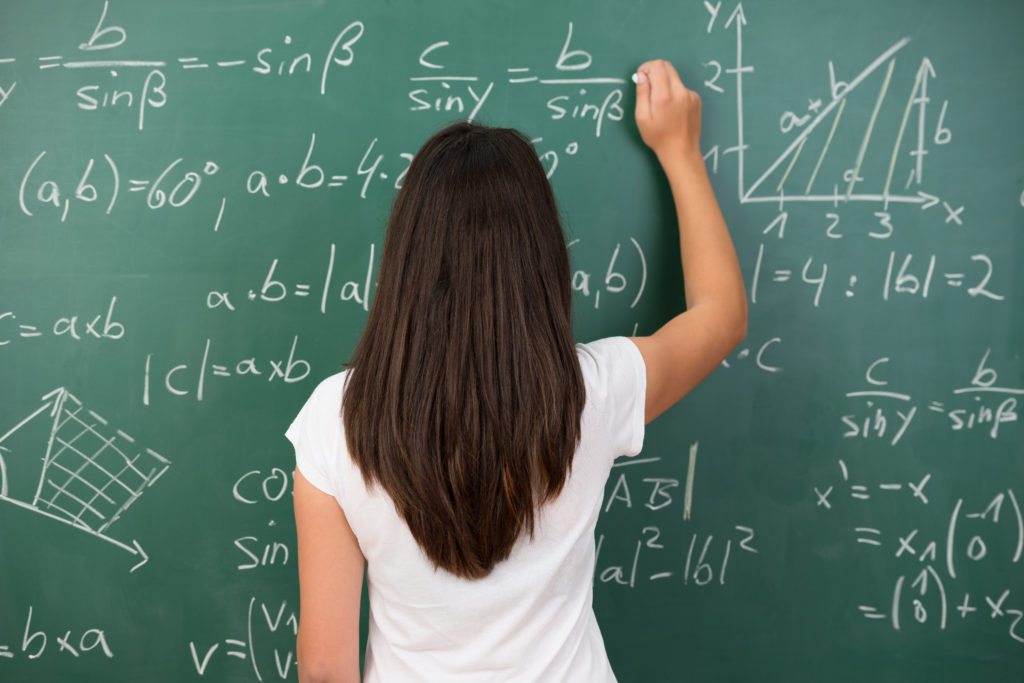 female student solving math problem on green chalkboard | san antonio math include