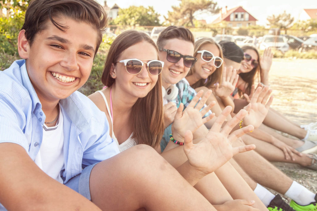 group of teens sitting on curb outside during summer wearing sunglasses