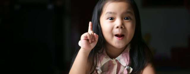 preschool girl raising hand with finger and surprised smile on her face